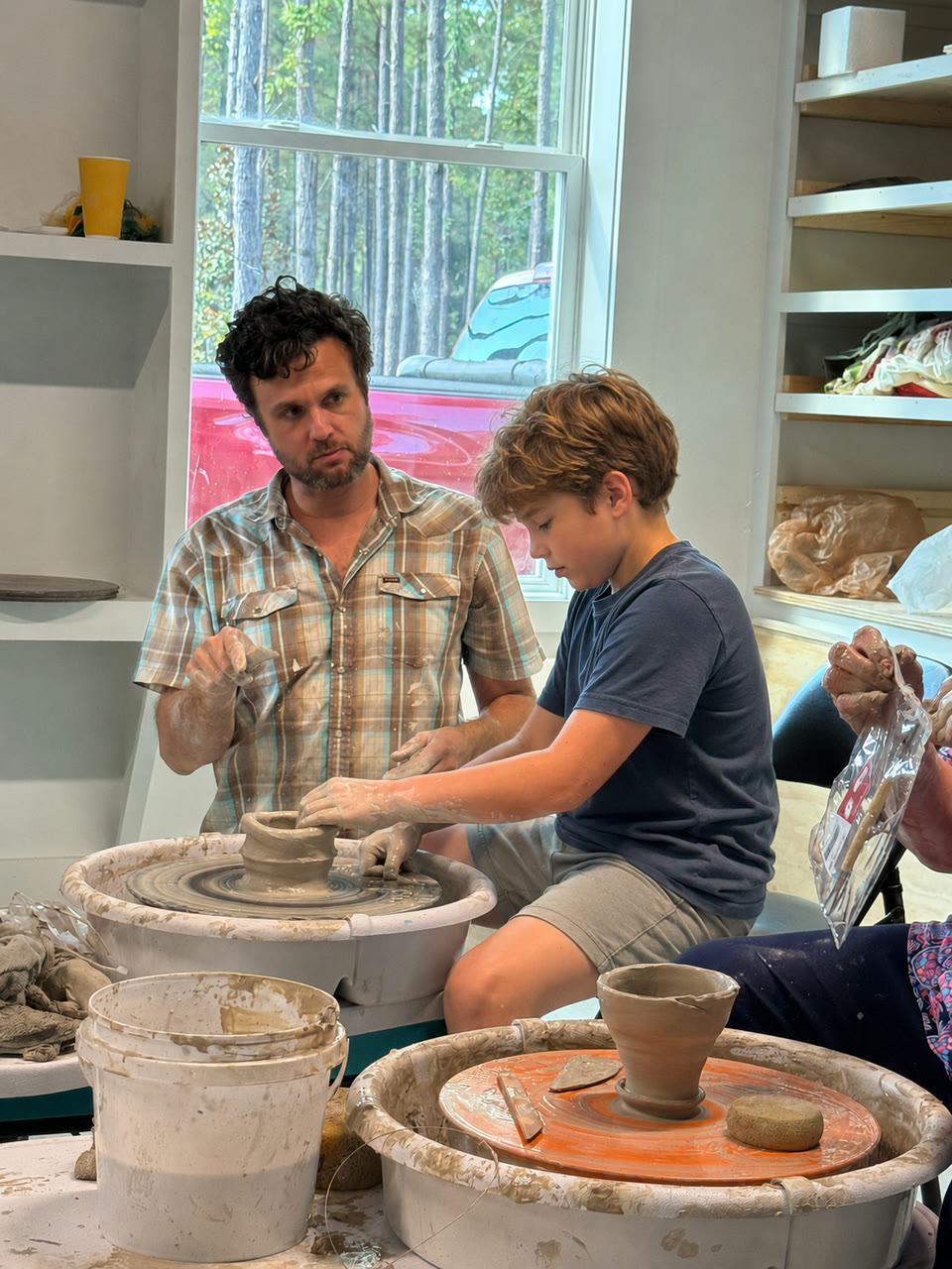 An instructor helping a child shape clay at a pottery wheel