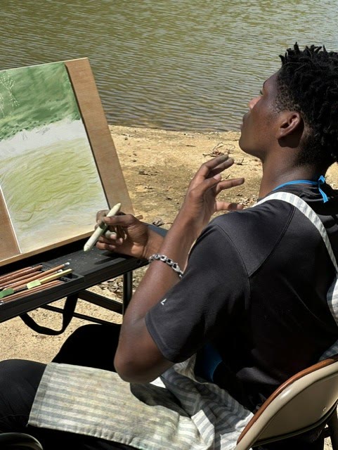 An artist drawing and painting beside the water at Riverhouse Create