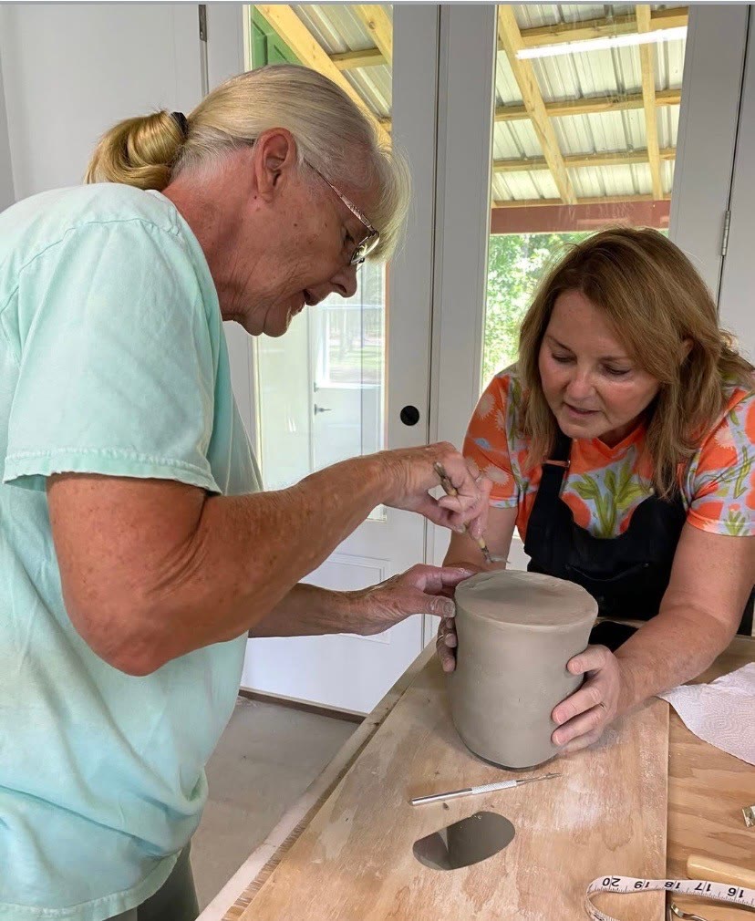 Two potters shaping a clay vessel together at Riverhouse Create