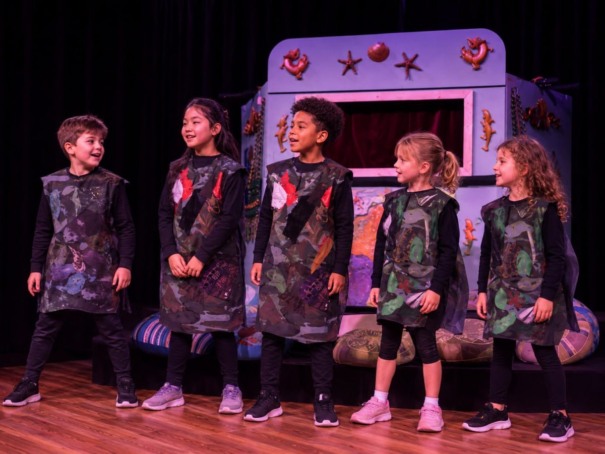 The company mid-scene, in a line in front of the painted set.