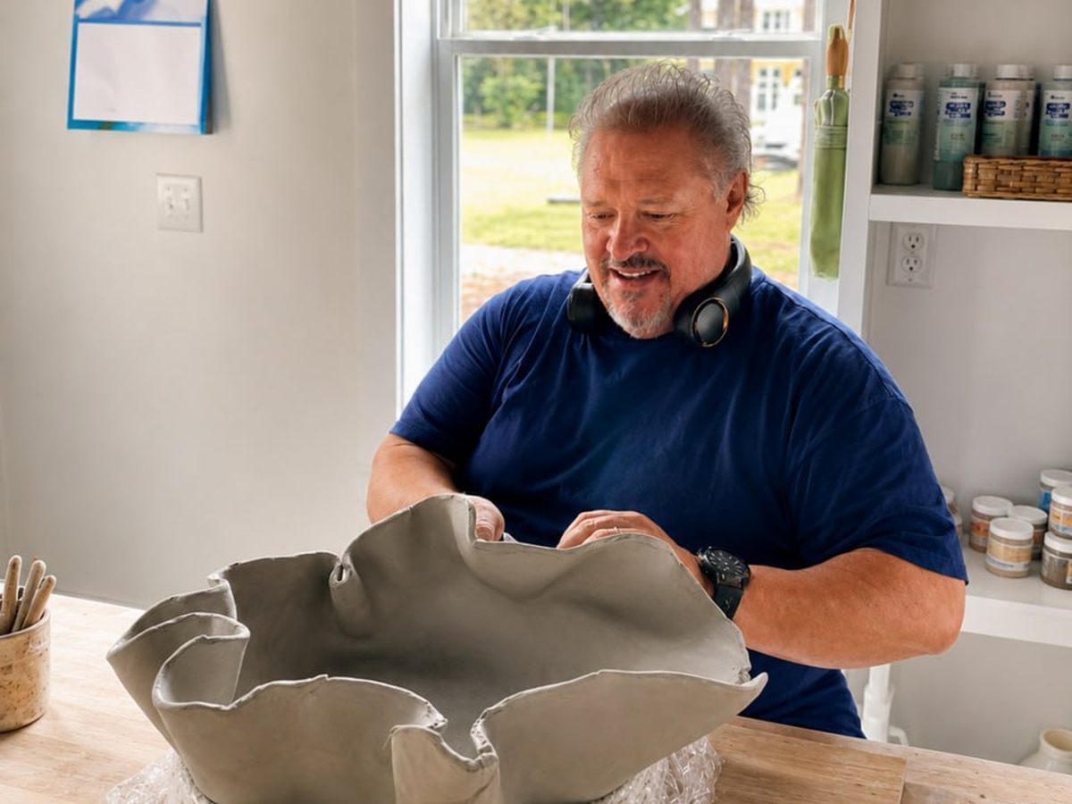 A potter smiling at the wide ruffled clay bowl he has just built by hand