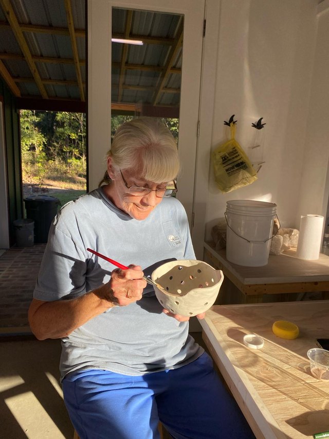 A potter painting glaze onto a finished bowl by the window.