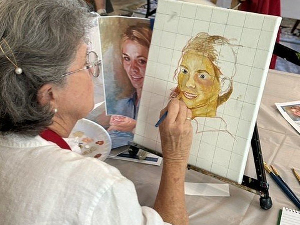 A painter at a table working a portrait in oils on a small canvas