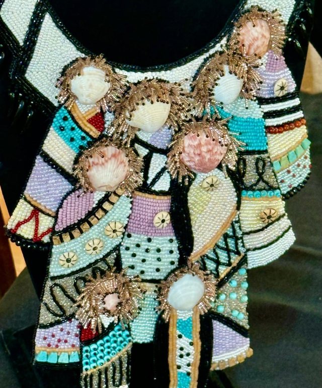 A beaded collar seen close up, worked in seed beads around small painted faces.