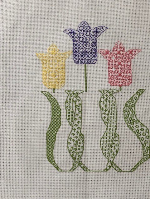 A cross-stitch panel of three tulips outlined in fine blackwork.