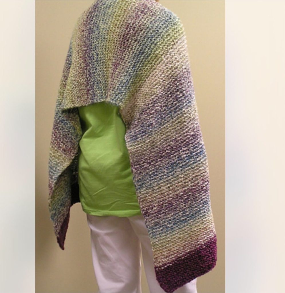 A knitted prayer shawl in soft blues, greens and plum, draped over someone’s shoulders.