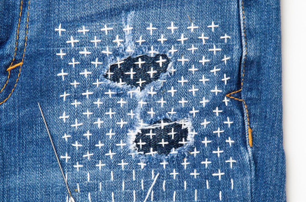 Two worn patches on denim mended with rows of white sashiko running stitch.