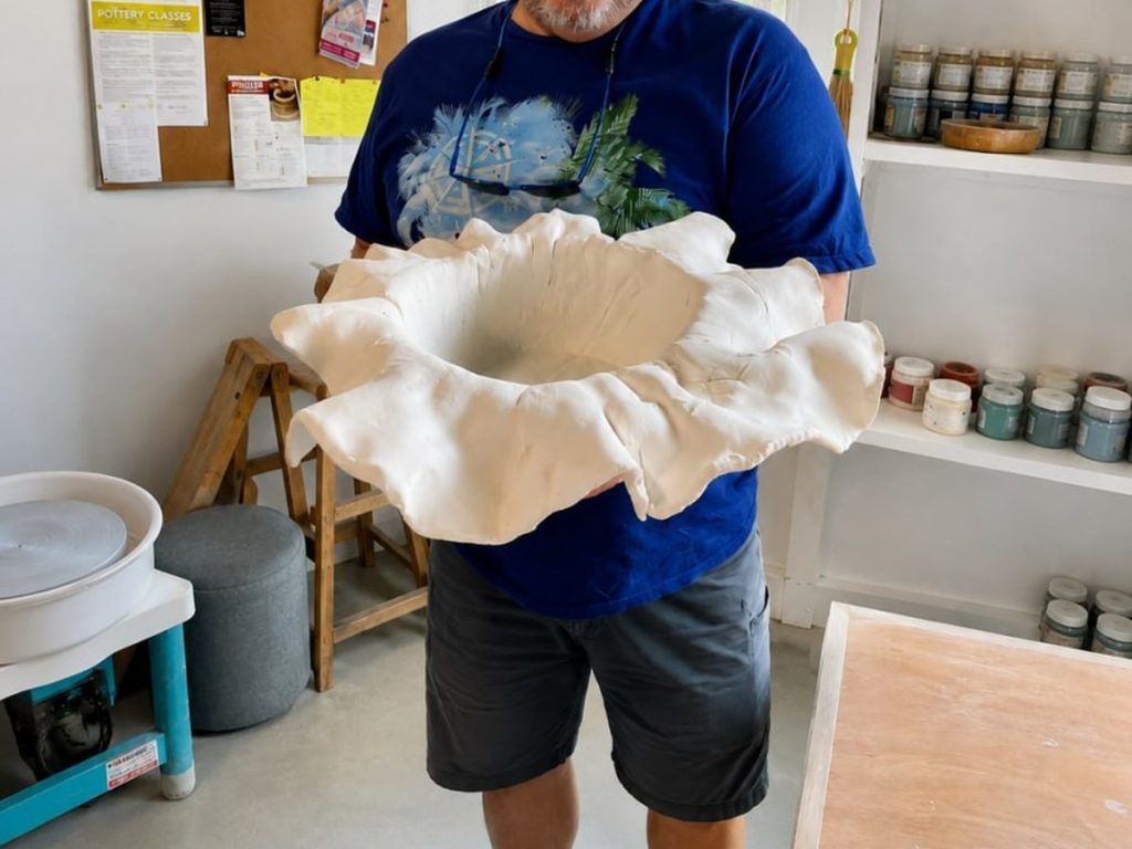 A potter carrying the finished ruffled bowl across the studio.