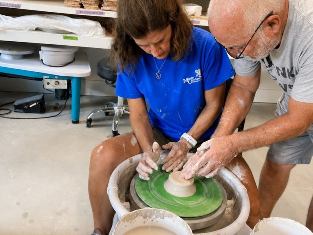 Two people working together, four hands on the wet clay.