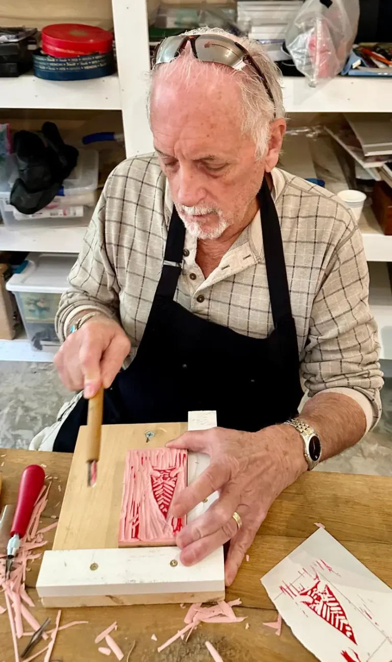 A man carves a linoleum block for printmaking at a table
