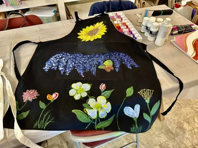 A hand-painted apron with sunflowers and wildflowers laid on a table