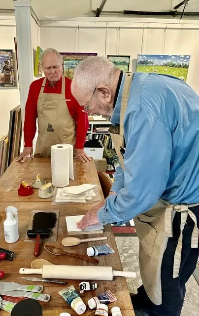 Two men work at a table covered with carving tools