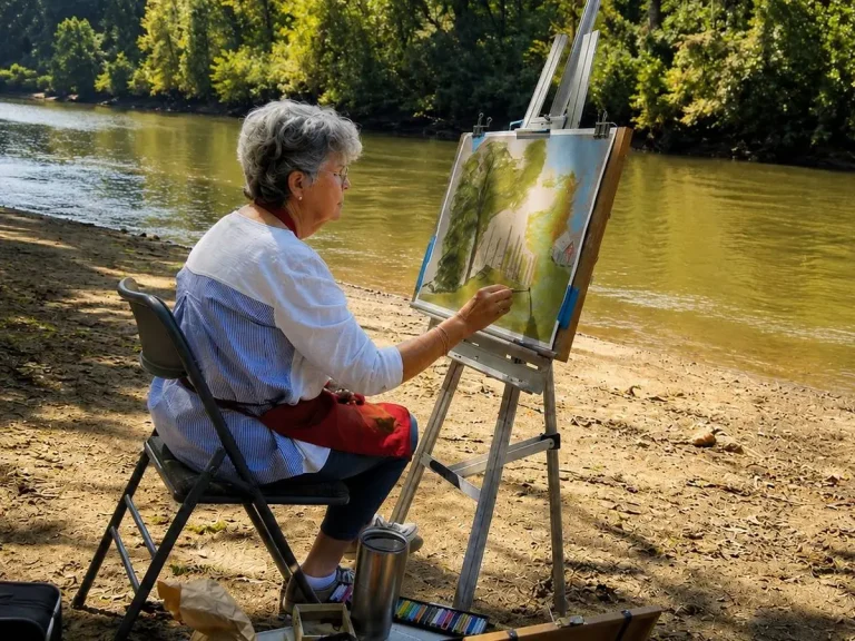 A painter, seated, faces the river from an easel