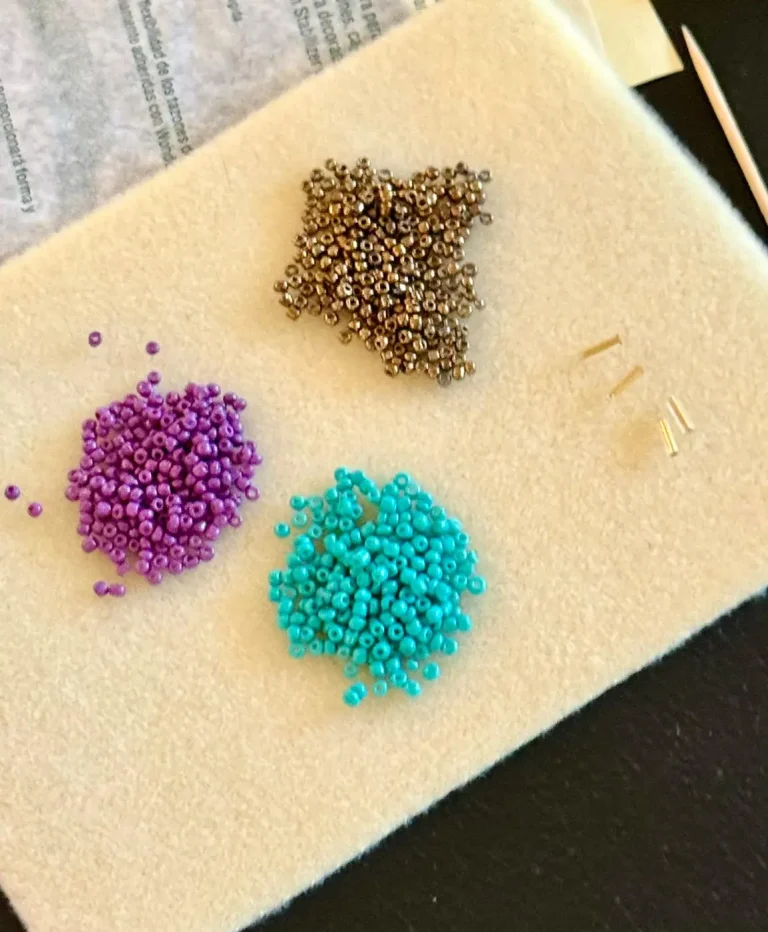 Piles of seed beads in purple, teal, and bronze on felt