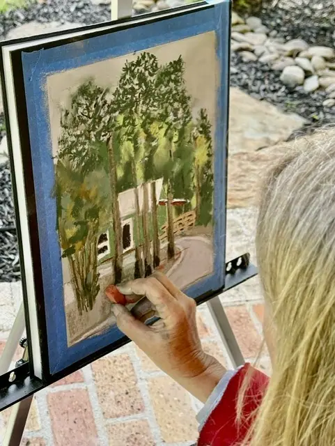 A painter works at an easel on a stone patio