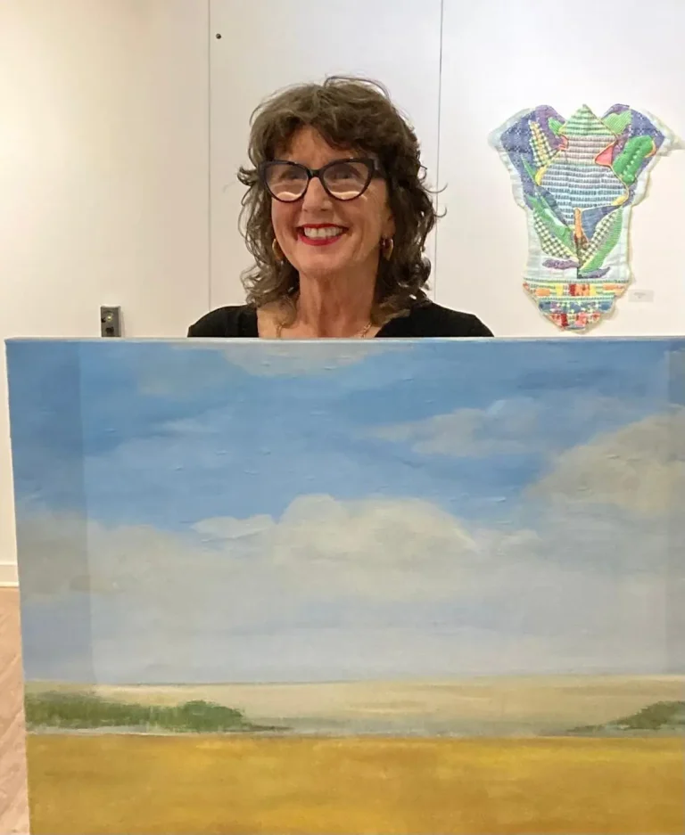 A woman poses with a landscape painting of sky and field