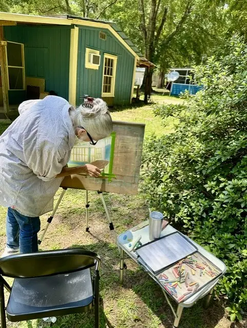 An artist paints outdoors near a green garden shed