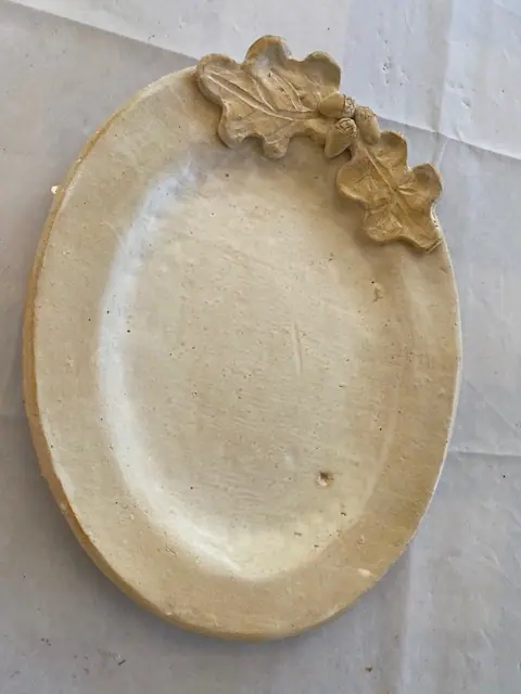 A cream-glazed ceramic plate with a leaf-shaped handle