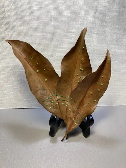 A ceramic magnolia leaf sculpture with a dotted glaze, on a stand