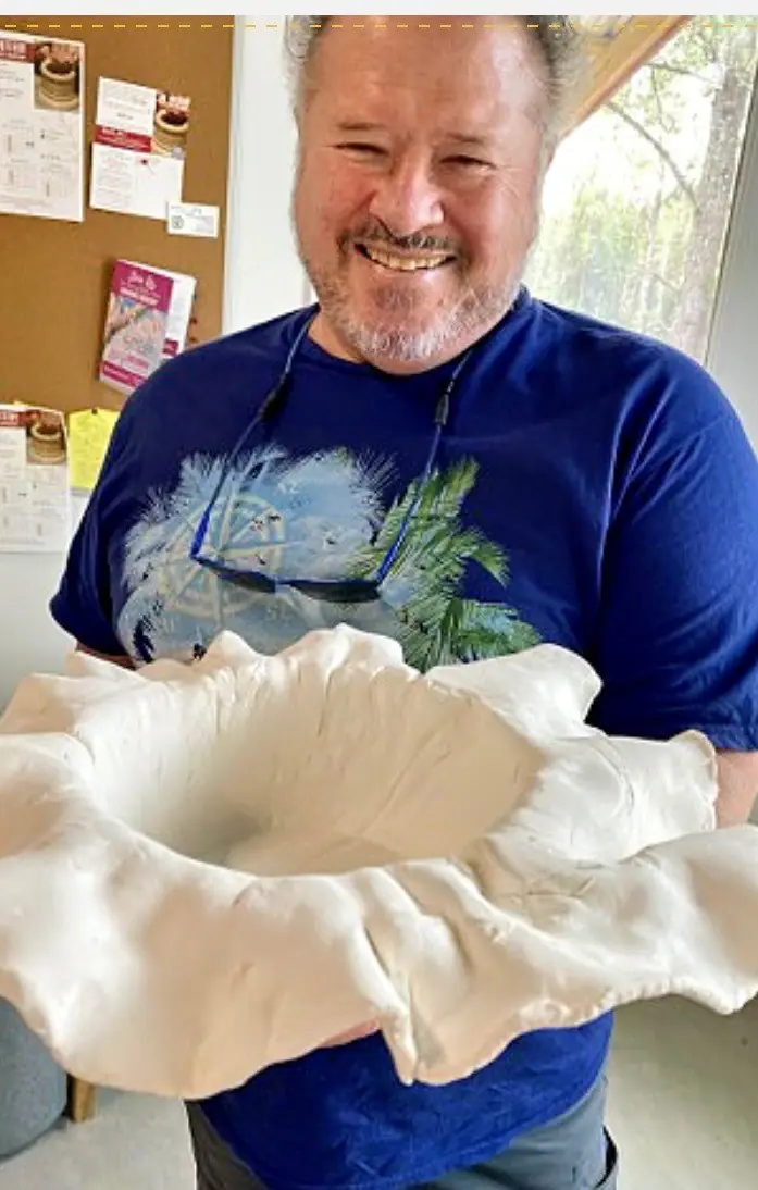 A potter holding a large hand-built clay bowl with a ruffled rim