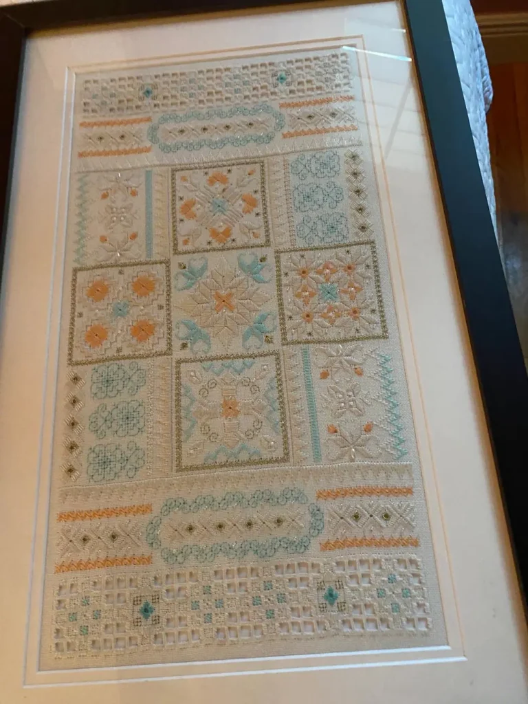 A cross-stitch sampler with pastel geometric patterns, framed