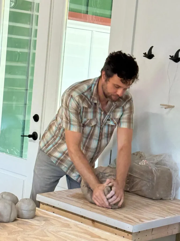 A potter wedging a ball of clay on a wood board
