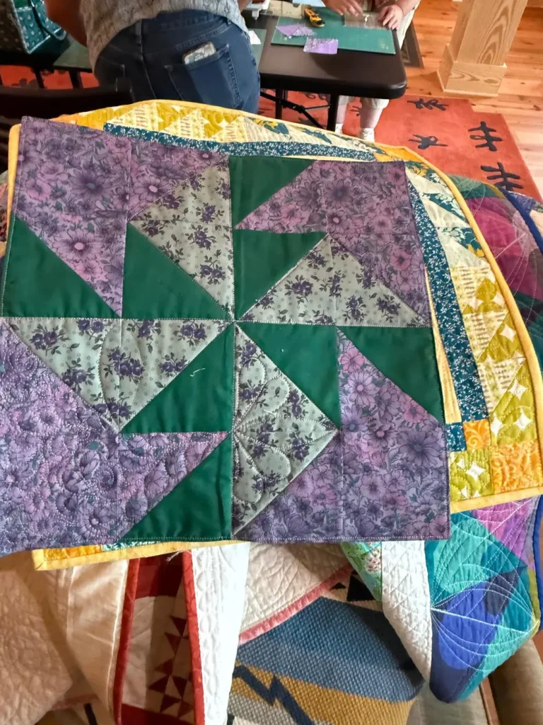 A green and purple pinwheel quilt draped over a chair