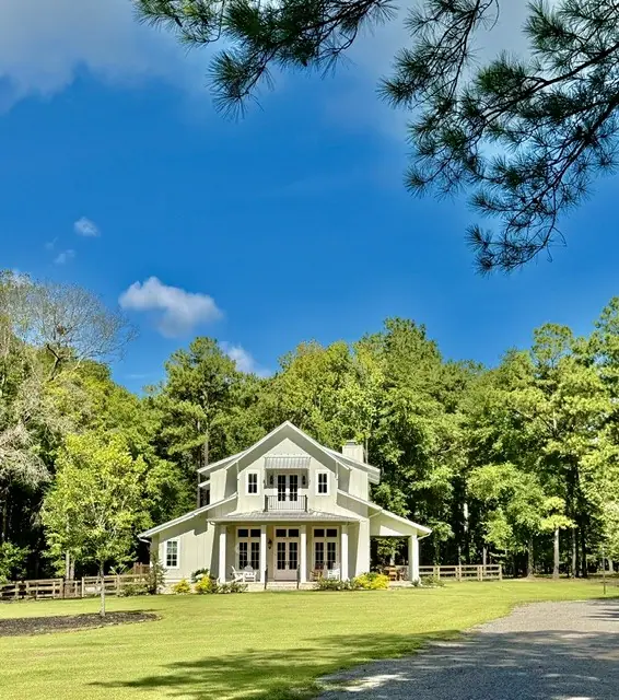 A white farmhouse with a wraparound porch under a blue sky