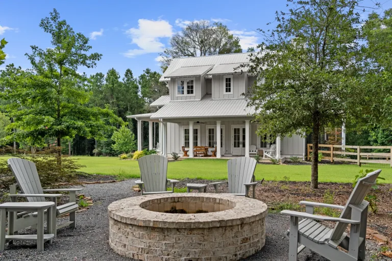 A stone fire pit and adirondack chairs on the farmhouse lawn