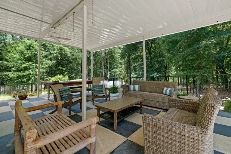 A covered porch with wicker furniture and a swing among trees